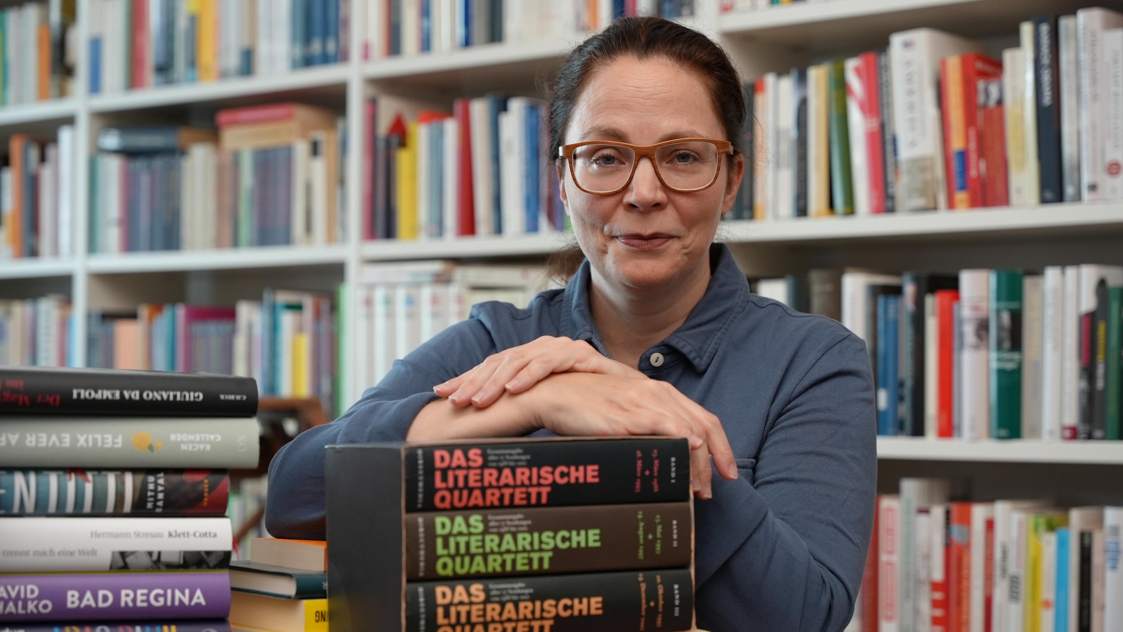 Thea Dorn lehnt an einem Bücherstapel