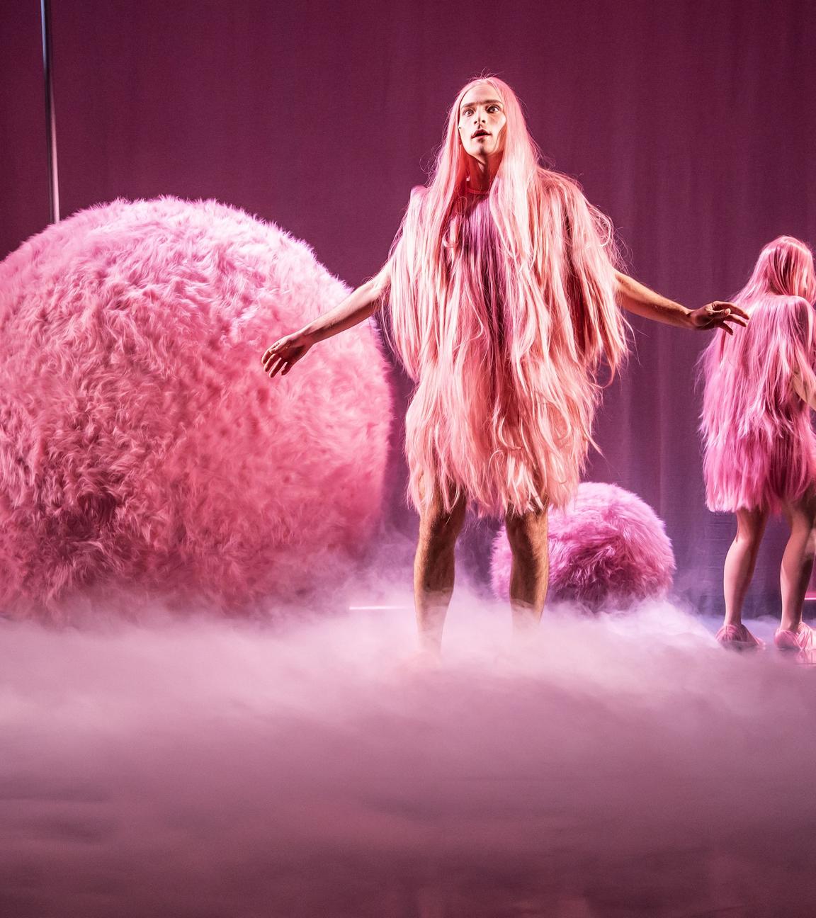 Bühnenszene: Zwei Personen mit rosa-farbenen Kostümen stehen zwischen großen rosa-farbenen Kugeln.