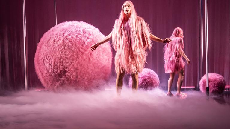 Bühnenszene: Zwei Personen mit rosa-farbenen Kostümen stehen zwischen großen rosa-farbenen Kugeln.