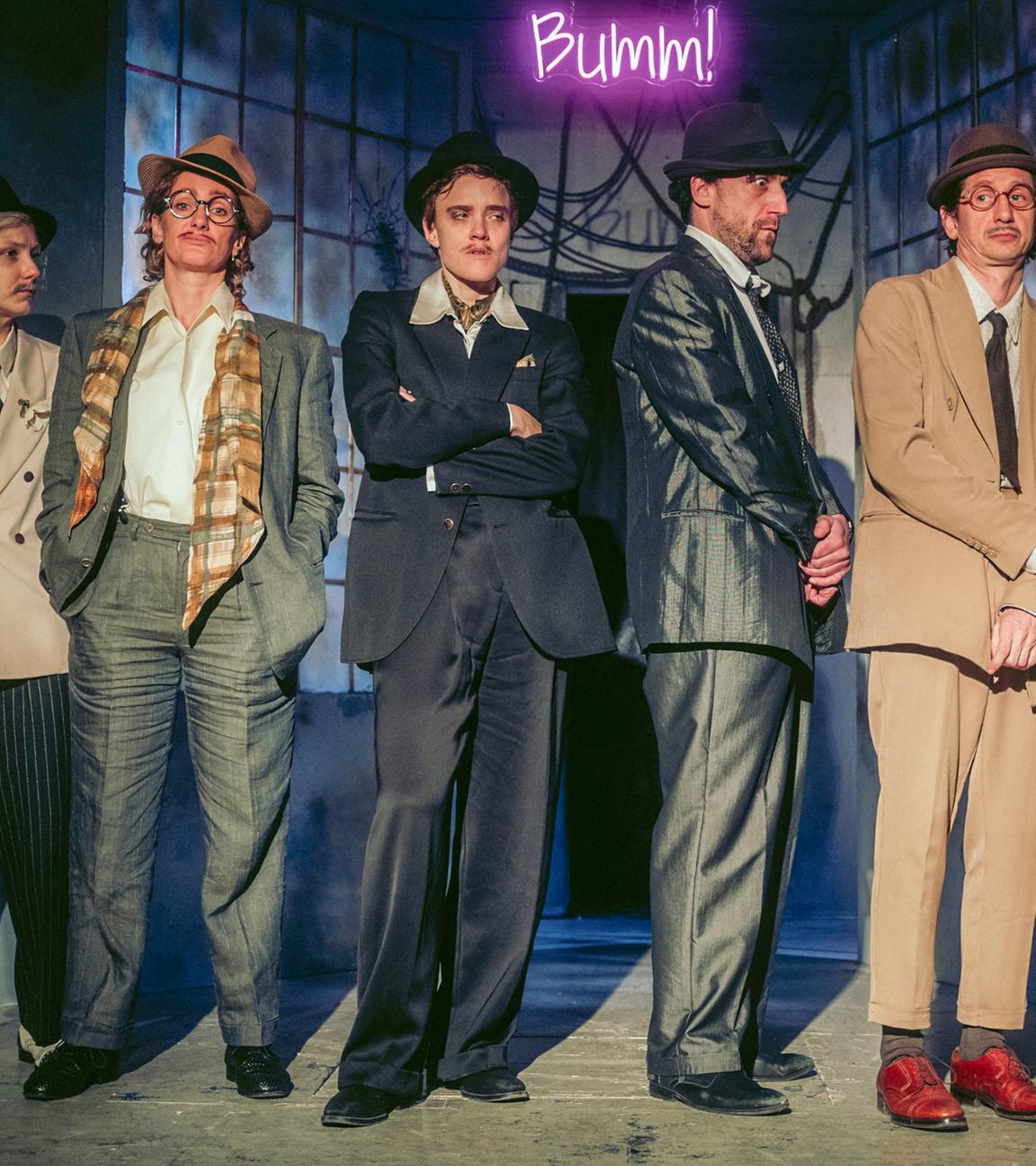 Fünf Personen mit Anzügen und Hüten bekleidet stehen auf der Bühne.