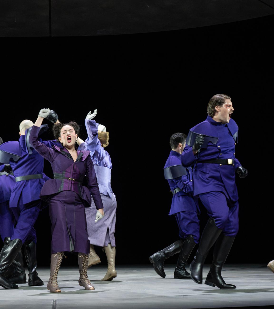 Bühnenszene: Menschen in violett-farbener Bekleidung tanzen auf einer Bühne.