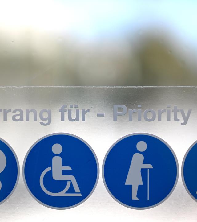 Piktogramme für Vorrang für Mütter/Väter mit Kinderwagen, Rollstuhlfahrerinnen und Rollstuhlfahrer, gebrechliche ältere Personen und sehbeeinträchtigte Personen, aufgenommen an einer U-Bahn Station in Wien.