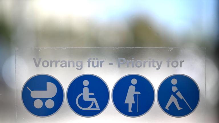 Piktogramme für Vorrang für Mütter/Väter mit Kinderwagen, Rollstuhlfahrerinnen und Rollstuhlfahrer, gebrechliche ältere Personen und sehbeeinträchtigte Personen, aufgenommen an einer U-Bahn Station in Wien.