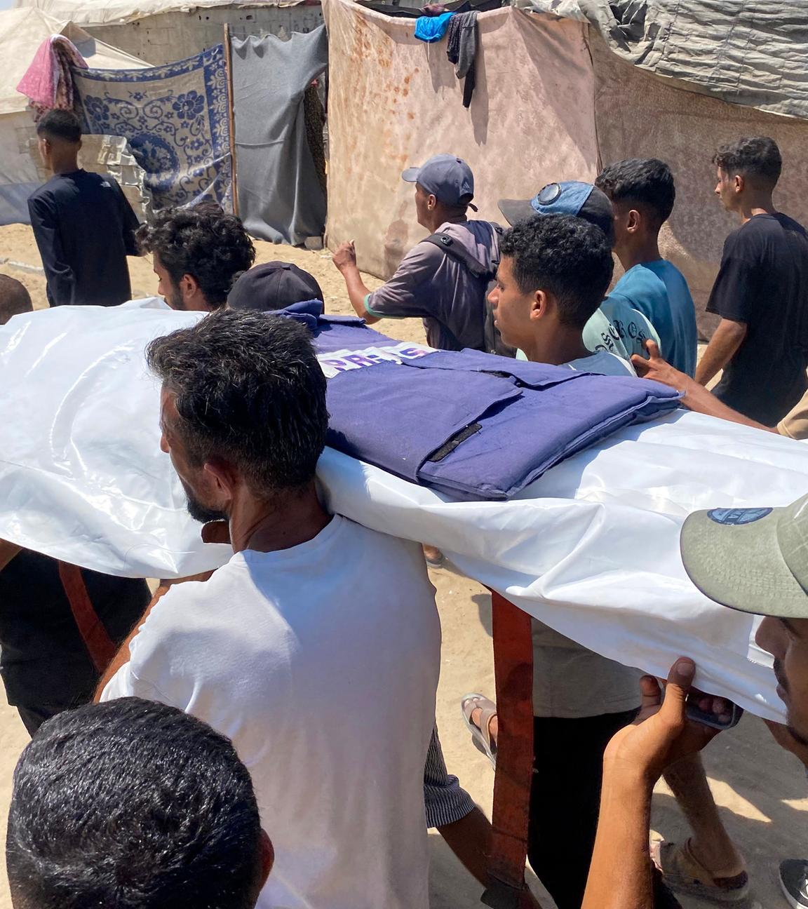 Mehrere Menschen in Gaza, wie sie einen mit einer Plane bedeckten, leblosen Körper tragen