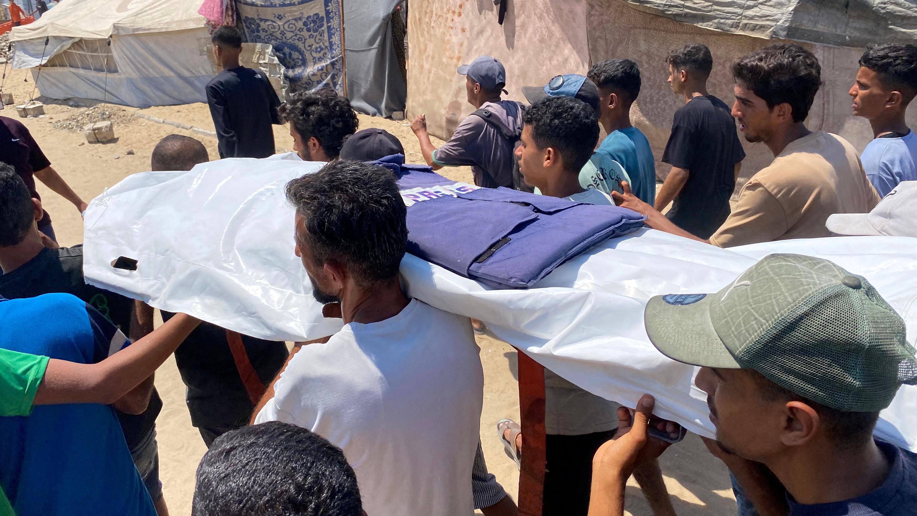 Mehrere Menschen in Gaza, wie sie einen mit einer Plane bedeckten, leblosen Körper tragen