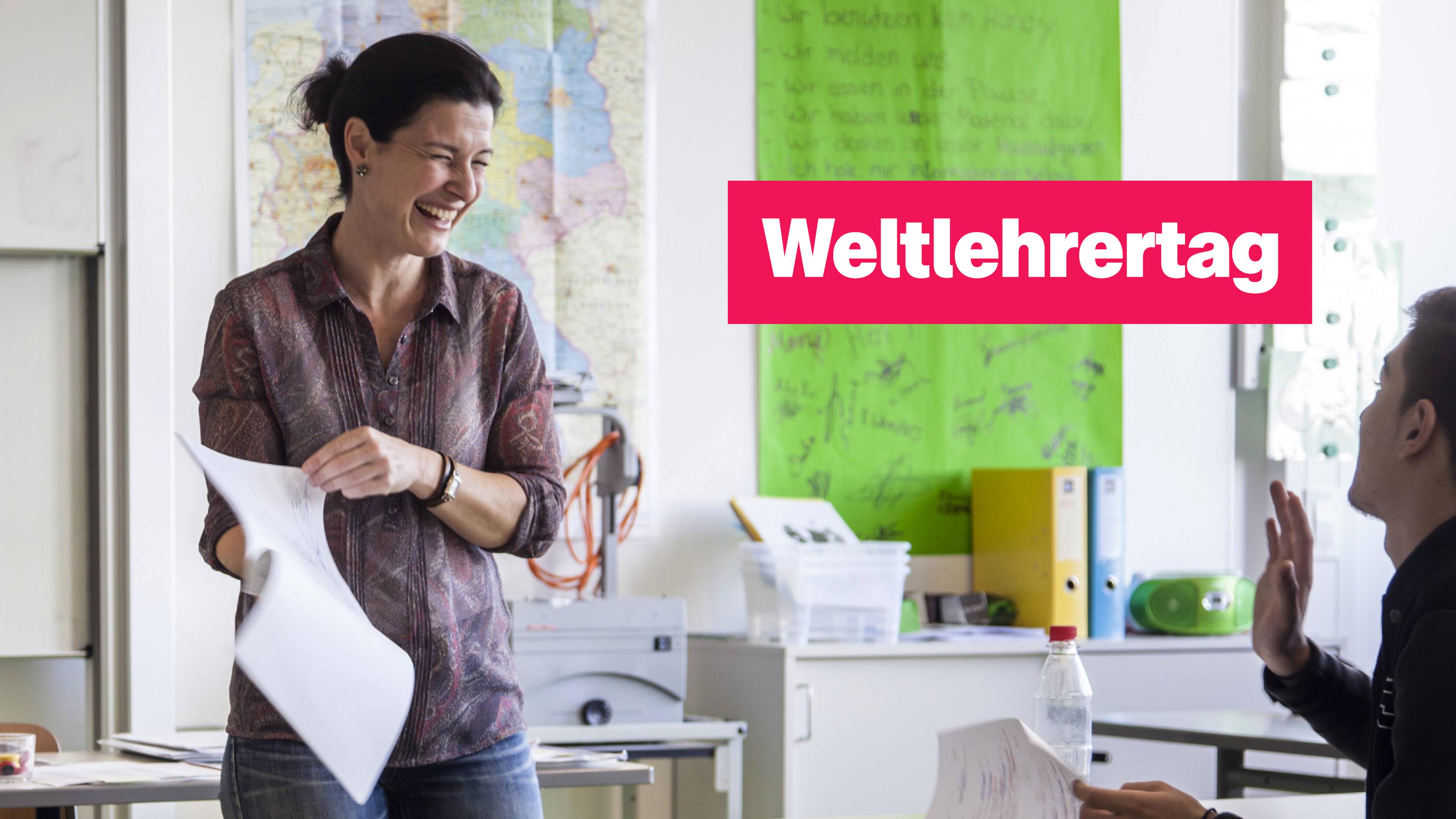 Eine Lehrerin mit Blättern in der Hand lacht einen Schüler an. Rechts der Text "Weltlehrertag".