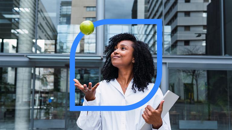 Lächelnde Geschäftsfrau, die einen Apfel nach oben wirft, im Hintergrund Bürogebäude