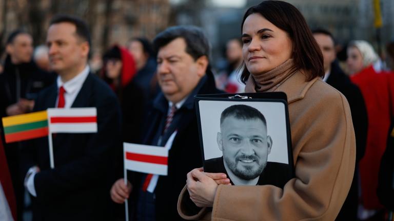 Belarussiche Oppositionsführerin Tichanowskaja hält Foto ihres Ehemanns während Feierlichkeit.
