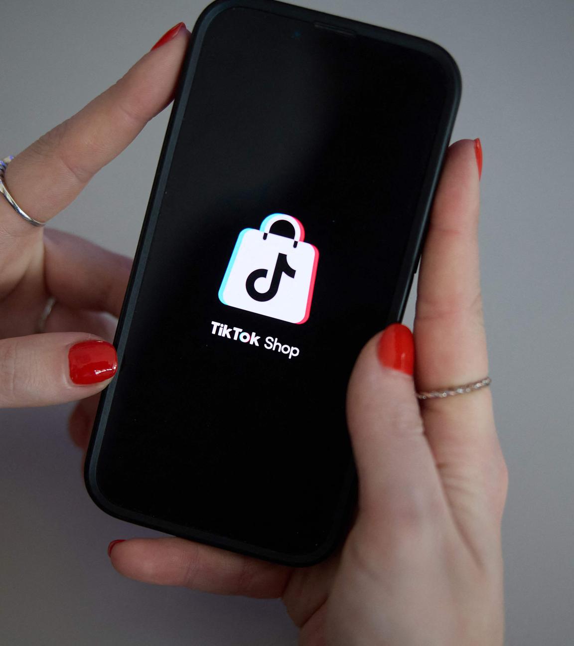 Zu sehen sind zwei Hände, die ein Handy halten. Auf dem Bildschirm ist das Appsymbol von Tiktok zu sehen und ein Schriftzug mit "Tik Tok Shop".