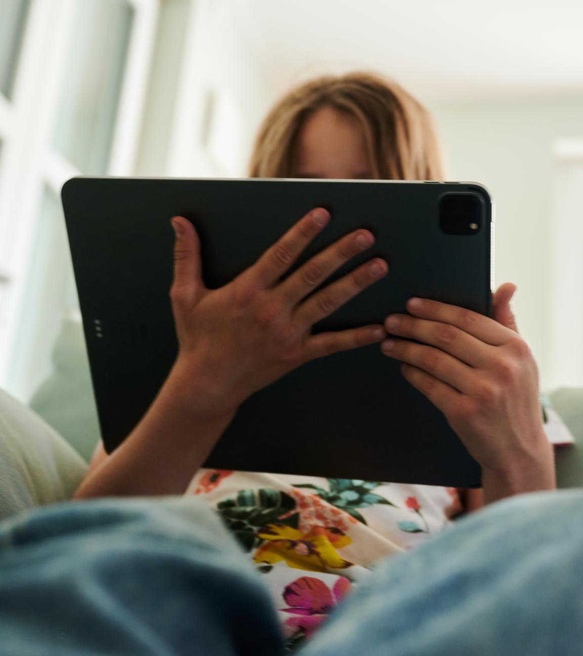 Ein Mädchen sitzt auf der Couch und guckt in das Tablet ihrer Eltern.
