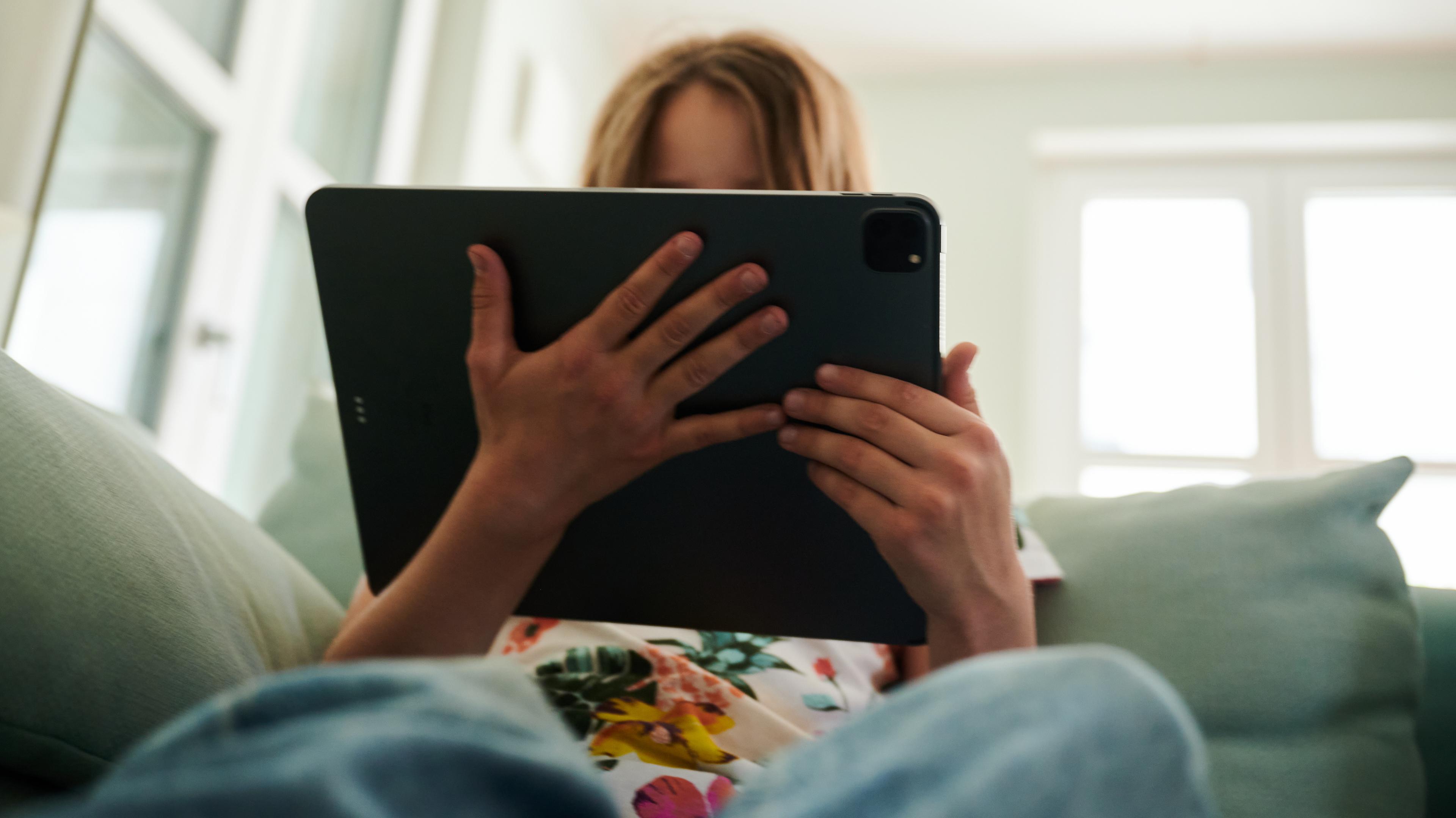 Ein Mädchen sitzt auf der Couch und guckt in das Tablet ihrer Eltern.