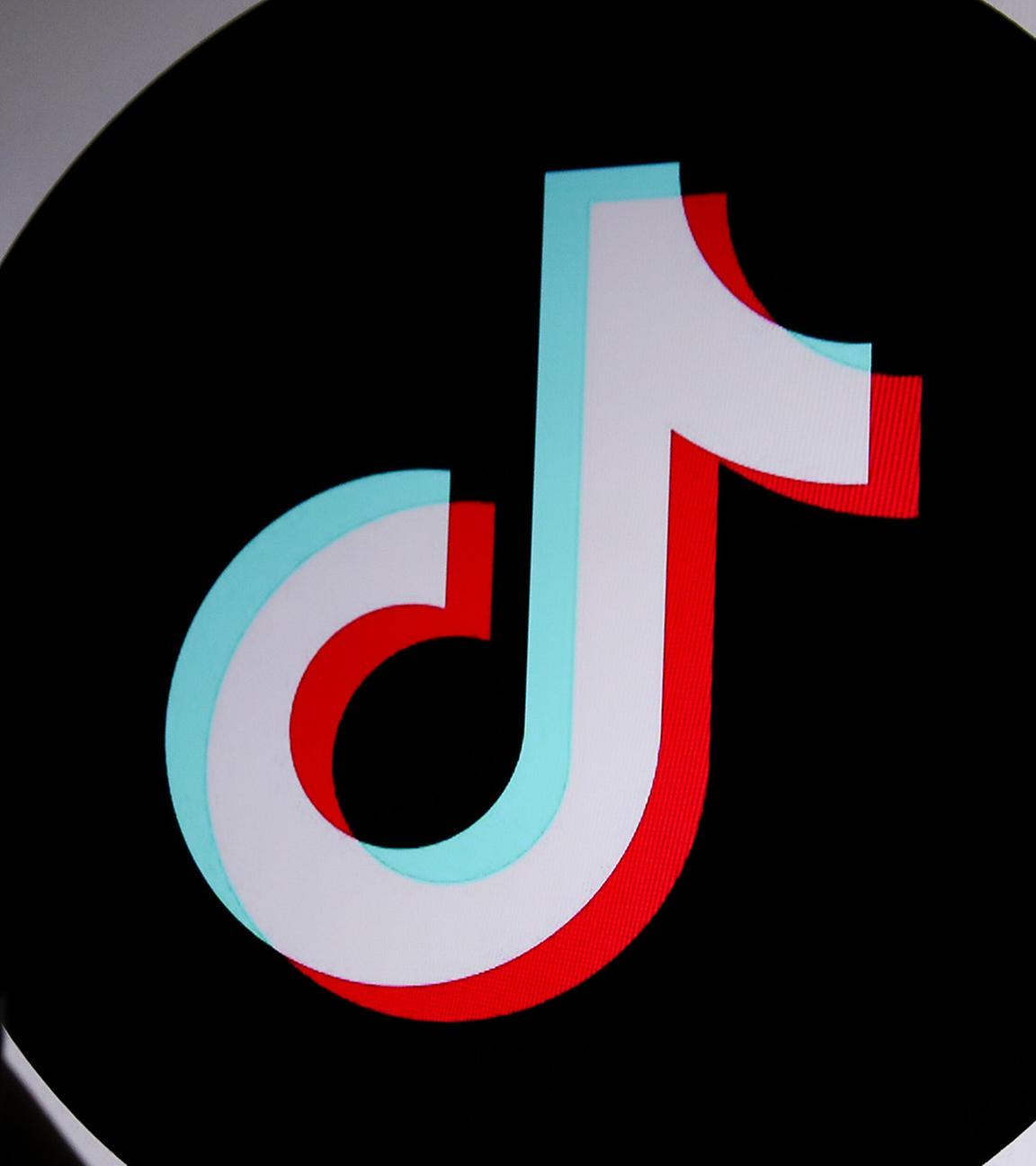 Eine junge Person hält ein Smartphone im Hintergrund ist das TikTok-Logo zu sehen.