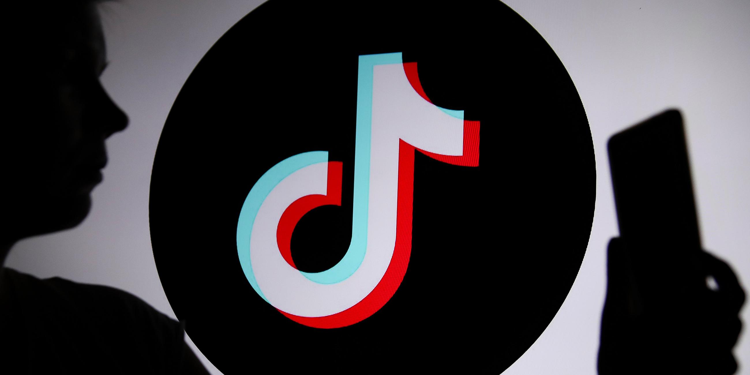 Eine junge Person hält ein Smartphone im Hintergrund ist das TikTok-Logo zu sehen.
