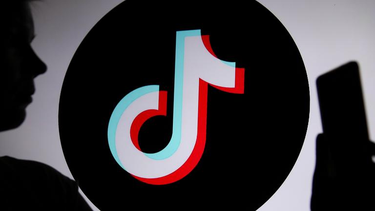Eine junge Person hält ein Smartphone im Hintergrund ist das TikTok-Logo zu sehen.