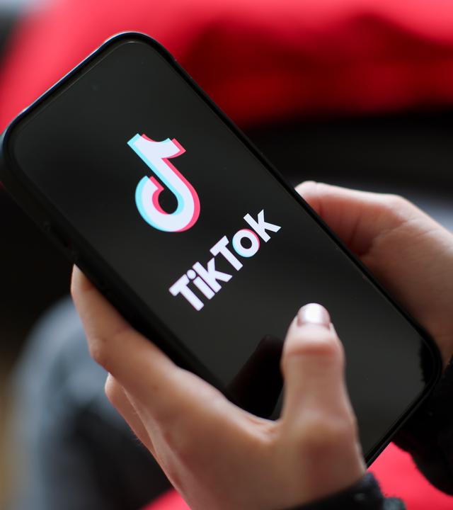 Ein Mädchen hält ein iPhone 16 in den Händen, auf dem das Logo der App TikTok zu sehen ist