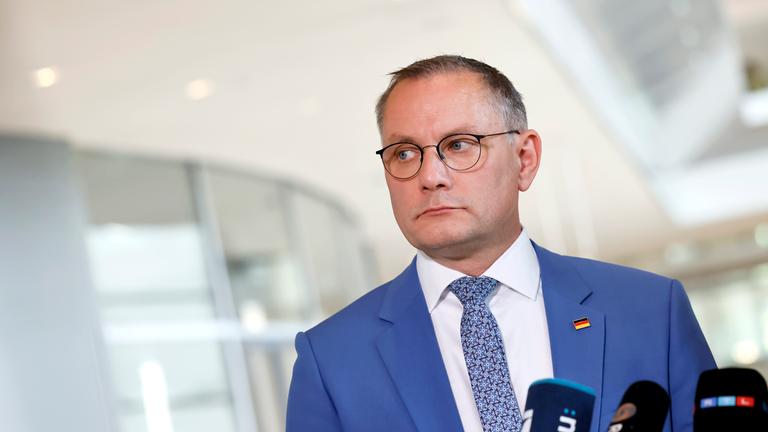 Tino Chrupalla von der AfD. Er trägt einen hellblauen Anzug mit einer Deutschlandflagge als Anstecker