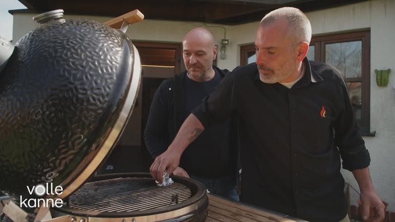 Zwei Männer stehen am Grill, den sie reinigen