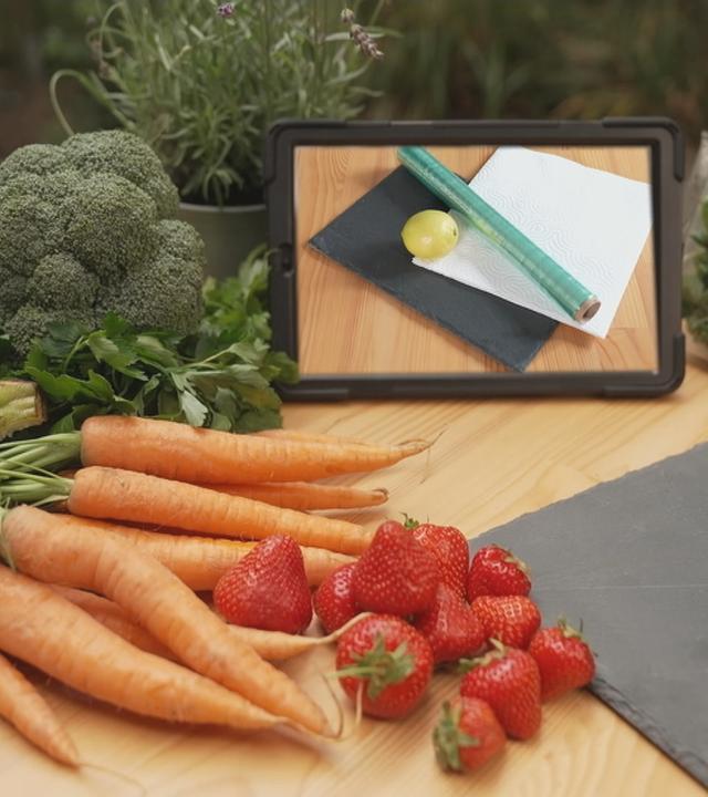 frisches Gemüse und Obst mit einer Zitrone, Küchenpapier und Frischhaltefolie im Hintergrund