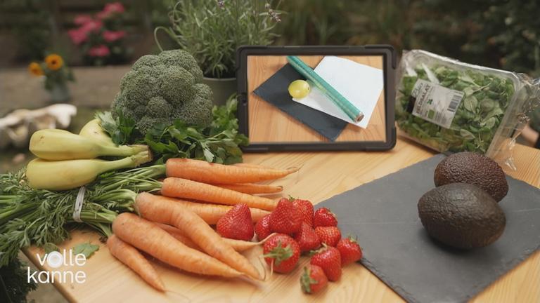 frisches Gemüse und Obst mit einer Zitrone, Küchenpapier und Frischhaltefolie im Hintergrund