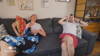 Ein Paar sitzt auf der Couch mit Fächer und Handtuch auf dem Kopf und will sich irgendwie abkühlen. 