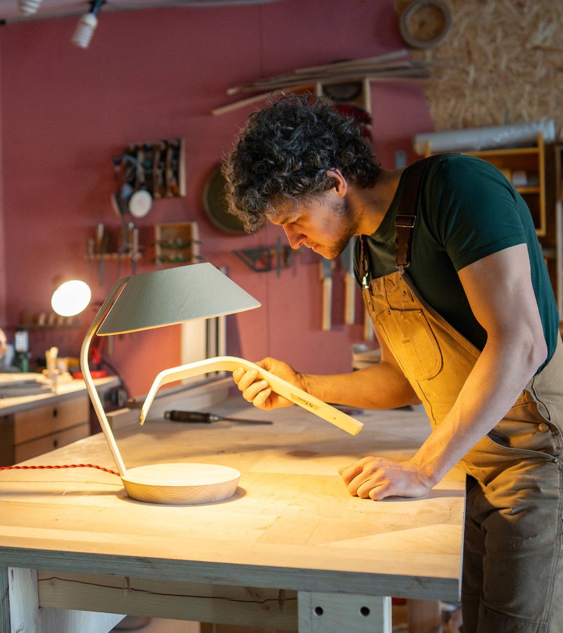 Ein männlicher Tischler arbeitet an einer Lampe in einer Tischlerei. (Archiv)