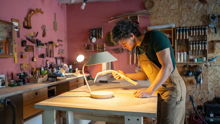 Ein männlicher Tischler arbeitet an einer Lampe in einer Tischlerei. (Archiv)