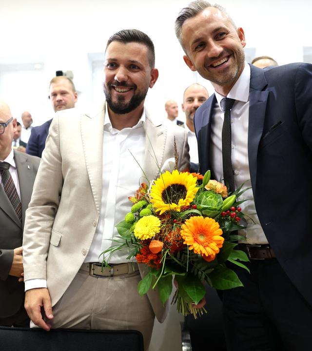 Tobias Rauch und Ulrich Siegmund lachen mit einem Blumenstrauß in der Hand