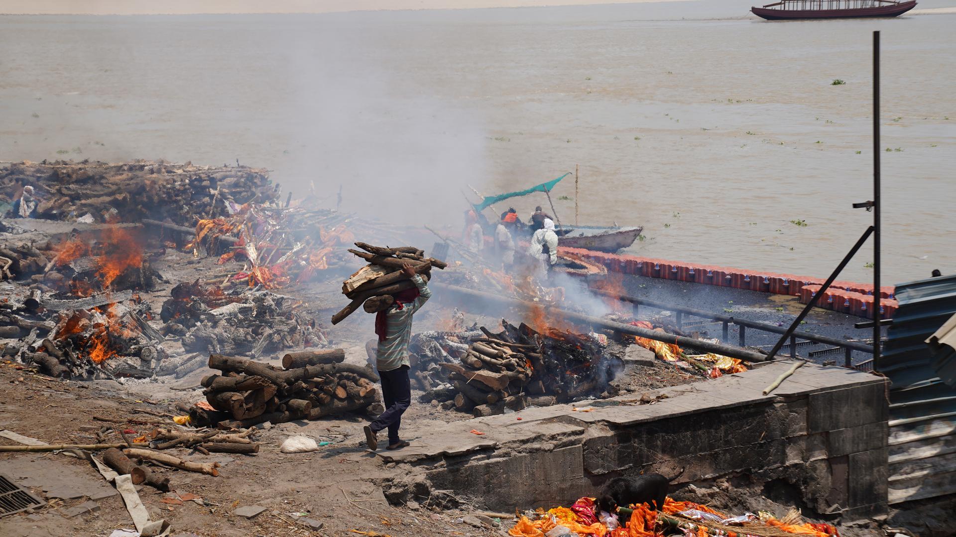 Indien, Varanasi: Ein Mann bringt mehr Holz zu Scheiterhaufen, wo Leichen beim Ganges verbrannt werden.