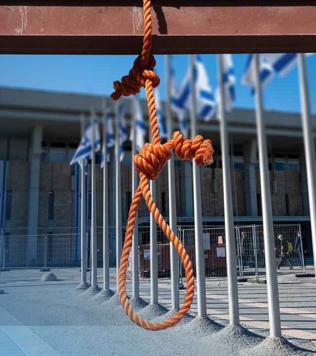 Man sieht eine Schlinge. In Hintergrund ein Gebäude mit der iraelischen Flagge.