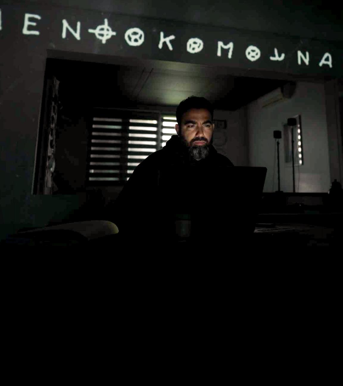 Rechts ein Mann vor dem Bildschirm seines Computers, über ihm auf die Wand projeziert Teile des Codes, den der Zodiackiller benutzt hat. Links das Phantombild des Zodiackillers auf einem Stapel alter Bilder, dahinter in rot sein Zeichen