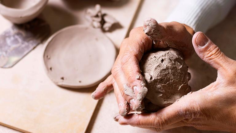 Ein Mann hält ein Stück Ton zwischen den Händen und formt es.