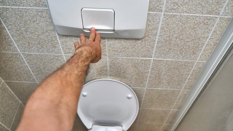Ein Mann betätigt die Toilettenspülung.