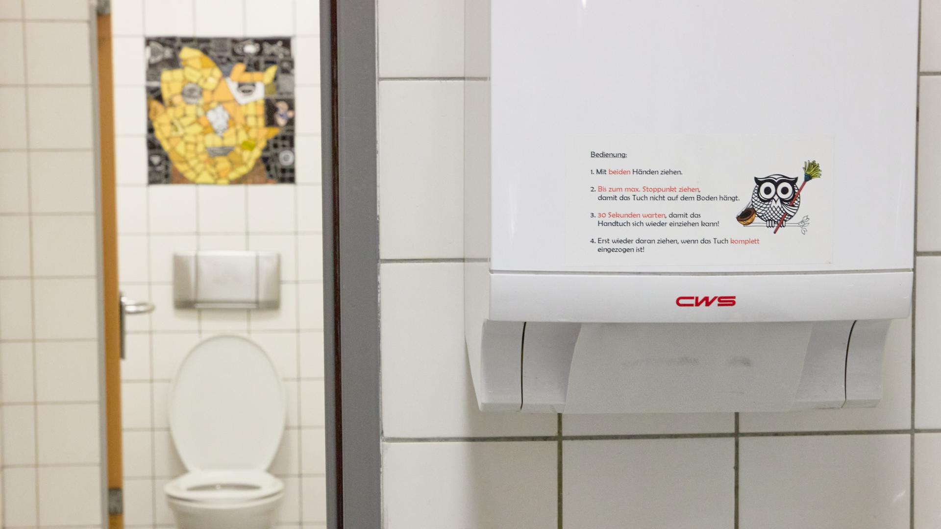 Ein eigens entwickelter Sticker, der die Handhabung erklärt, ist an einem Stoffhandtuchspender in einer Toilette des Gymnasiums Winsen zu sehen.