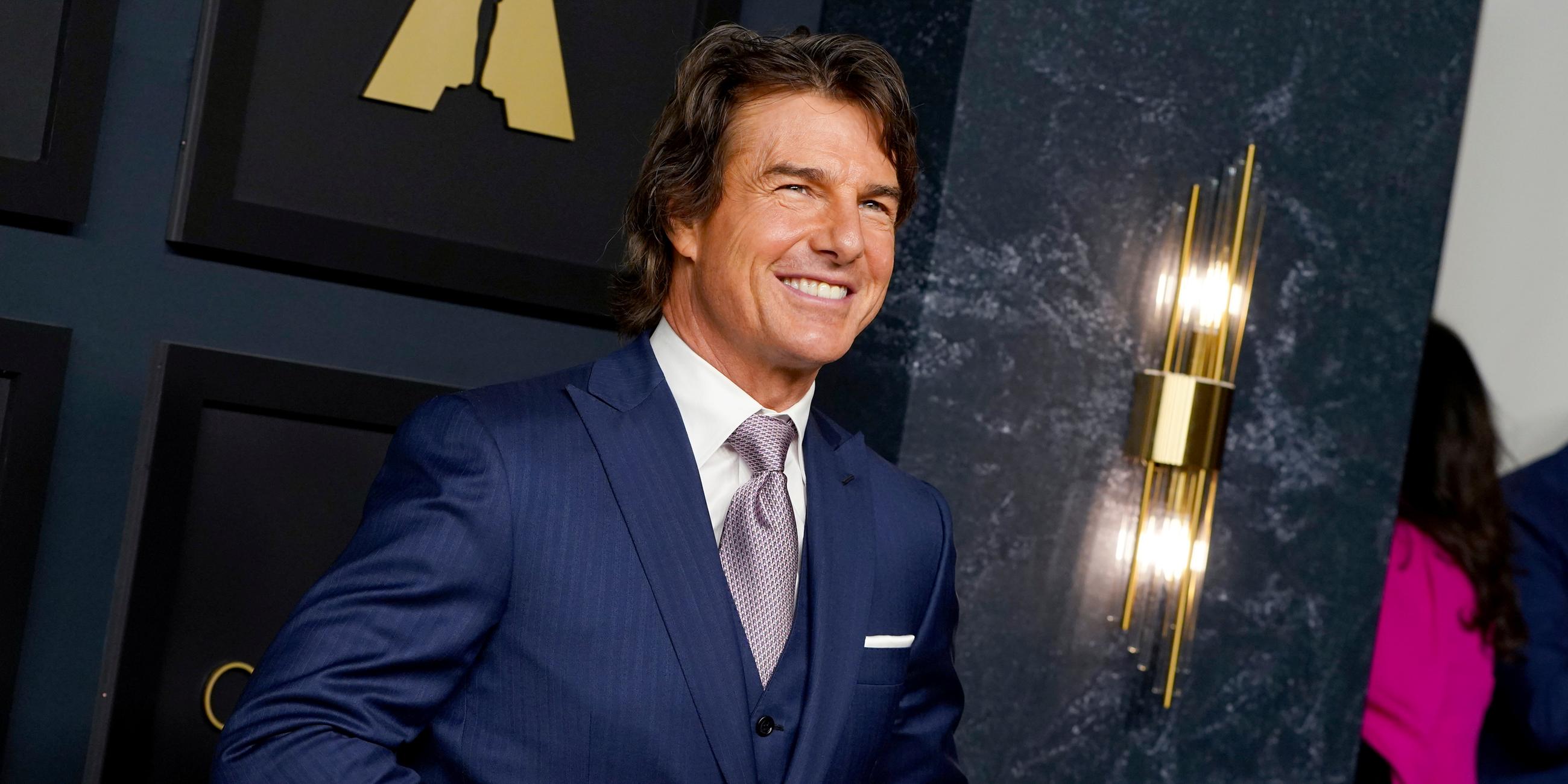 Tom Cruise strahlt und knüpft währenddessen sein dunkelblaues Jacket zu. 