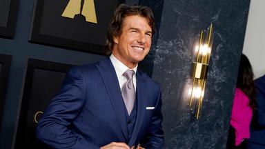 Tom Cruise strahlt und knüpft währenddessen sein dunkelblaues Jacket zu. 