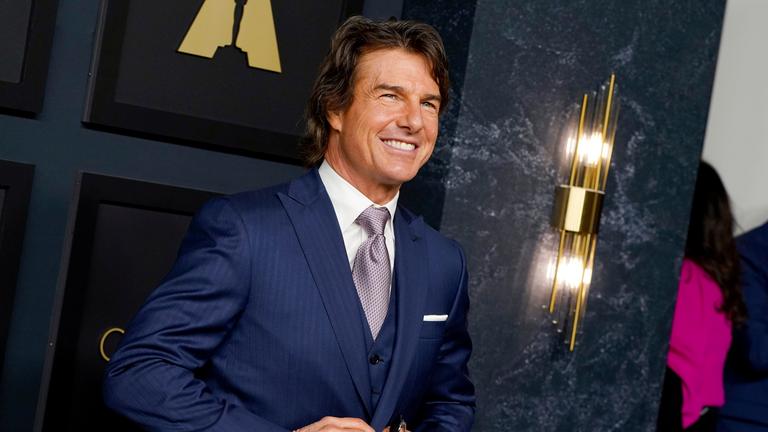 Tom Cruise strahlt und knüpft währenddessen sein dunkelblaues Jacket zu. 