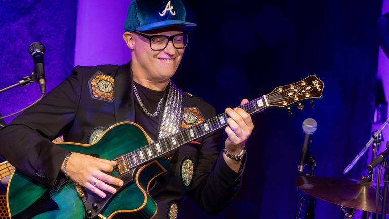Mann steht mit Gitarre auf der Bühne