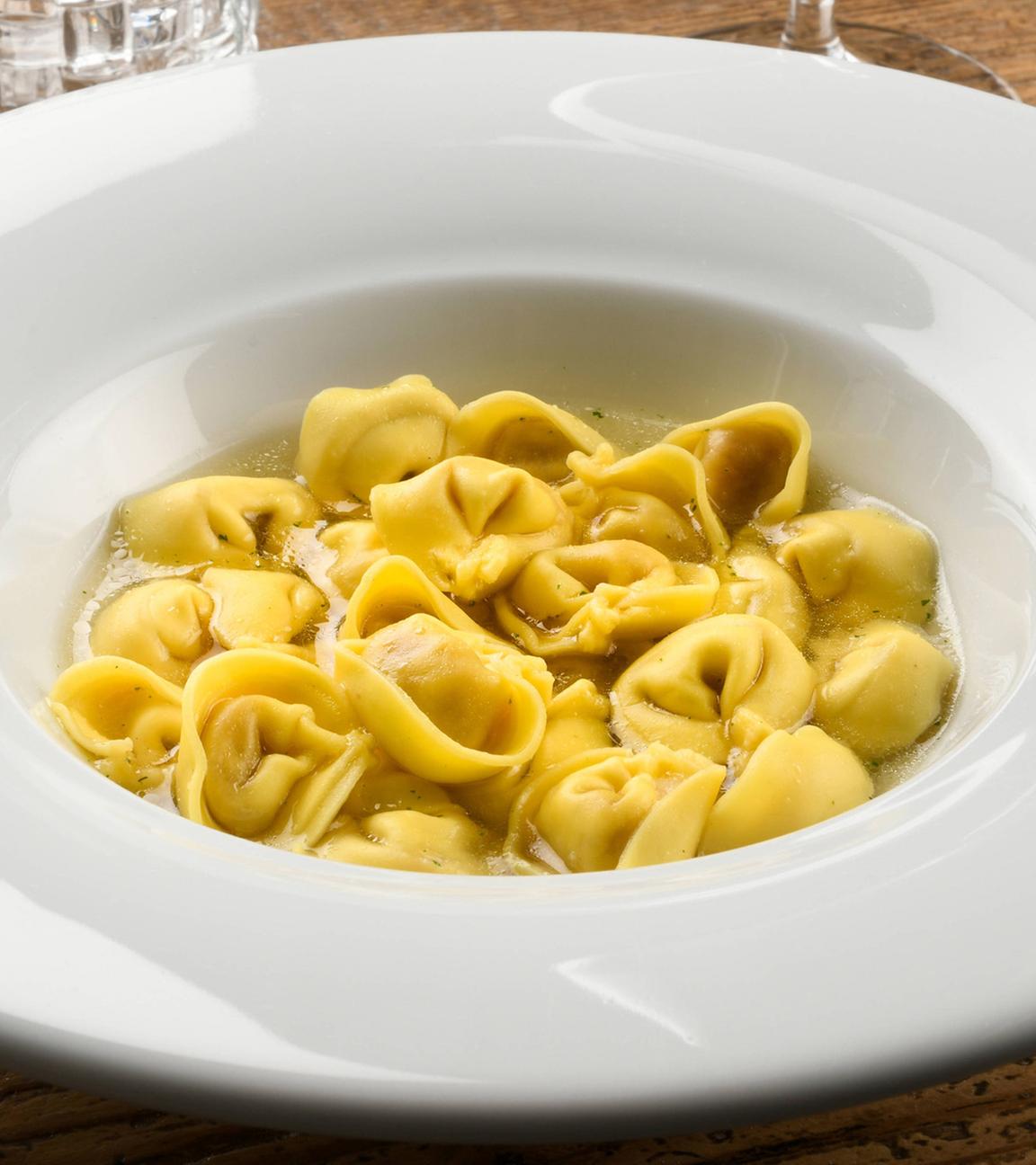 Schüssel mit Tortellini in Brühe aus der Region Emilia-Romagna in Italien, stilvoll in einem weißen Teller am Tisch serviert.