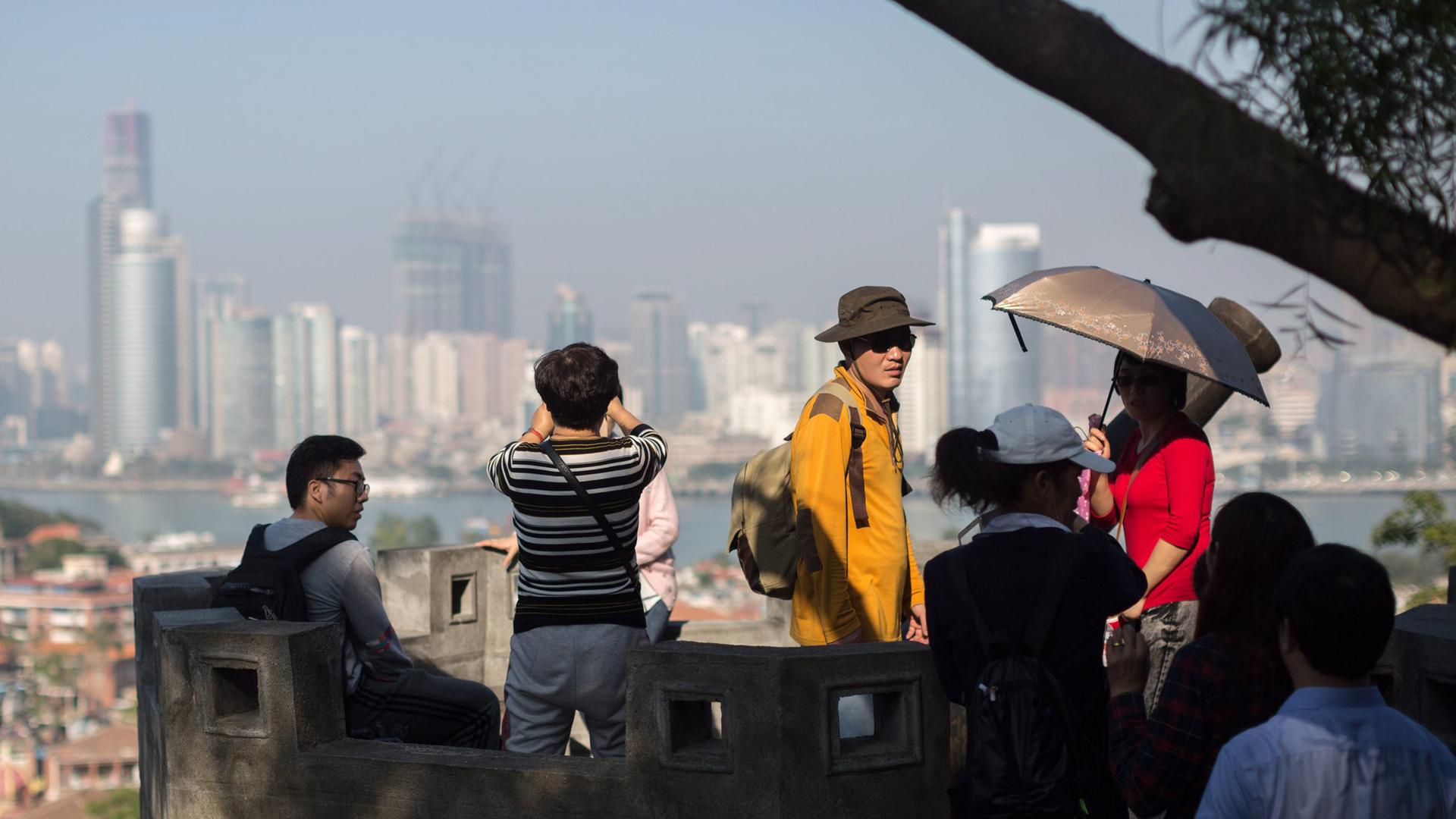 Touristen genießen den Panoramablick auf alte  Wohngebäude auf der Insel Gulangyu im Vordergrund und die moderne Skyline der Insel Xiamen im Hintergrund, Provinz Fujian, China. (Archivbild)