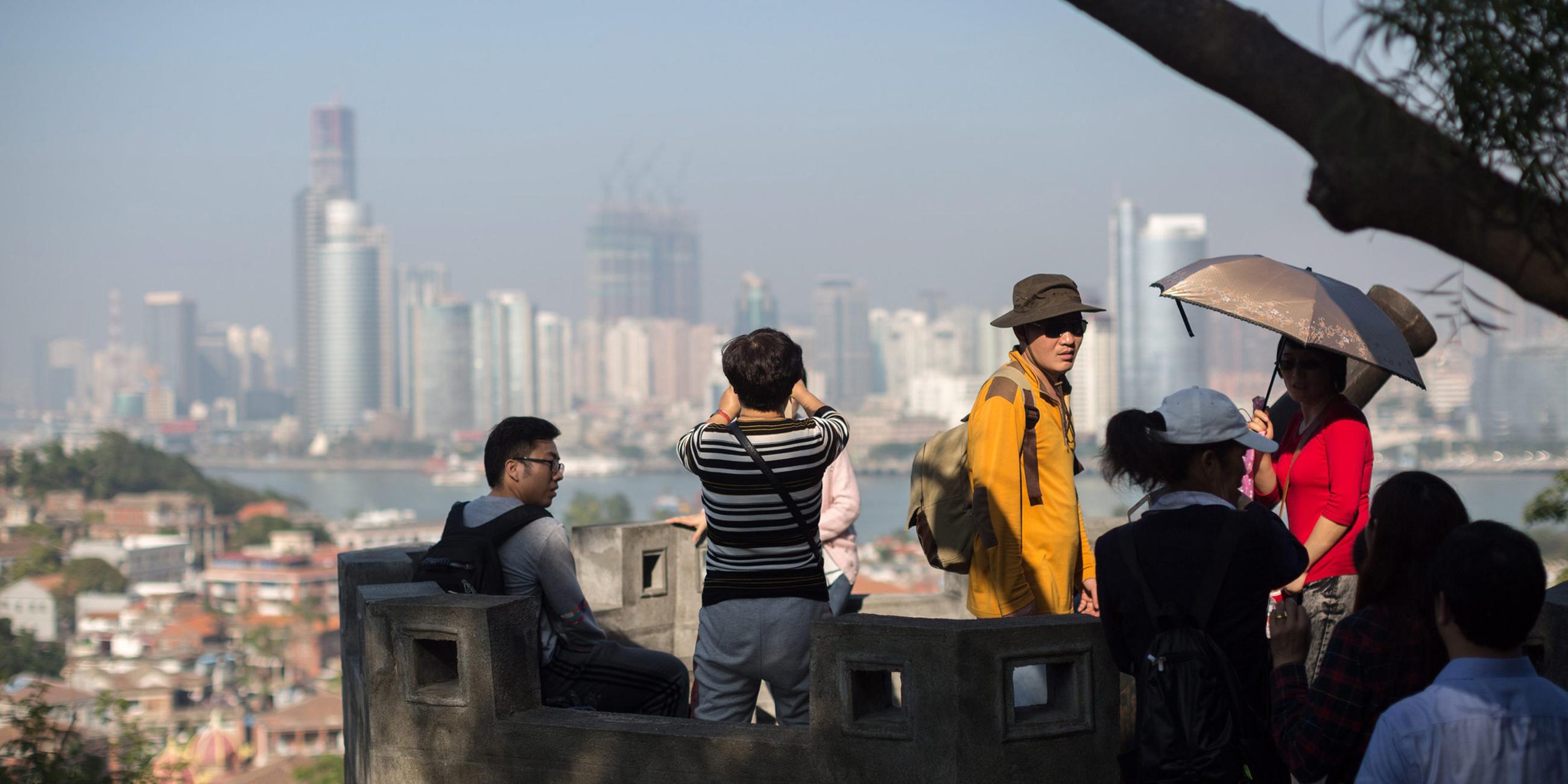 Touristen genießen den Panoramablick auf alte  Wohngebäude auf der Insel Gulangyu im Vordergrund und die moderne Skyline der Insel Xiamen im Hintergrund, Provinz Fujian, China. (Archivbild)