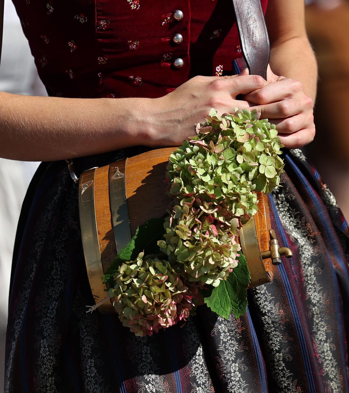 Eine Frau in einem Dirndl trägt ein Fass und eine Hortensienblüte.