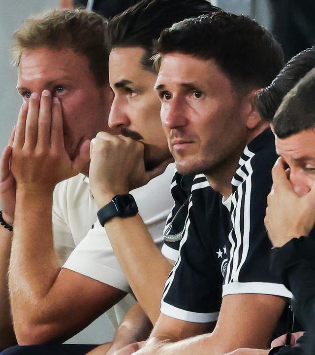 Bundestrainer Julian Nagelsmann (Deutschland, l-r), Assistenztrainer Benjamin Hübner (Deutschland), Assistenztrainer Benjamin Glück (Deutschland) und weitere Teammitglieder sitzen auf der Bank und verfolgen das Spiel.