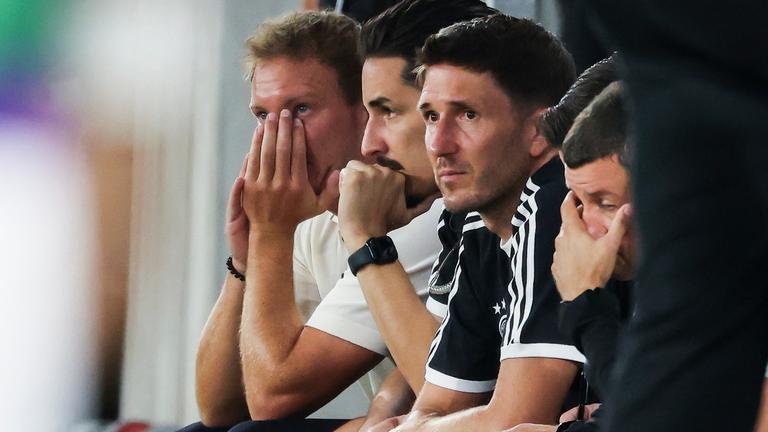 Bundestrainer Julian Nagelsmann (Deutschland, l-r), Assistenztrainer Benjamin Hübner (Deutschland), Assistenztrainer Benjamin Glück (Deutschland) und weitere Teammitglieder sitzen auf der Bank und verfolgen das Spiel.