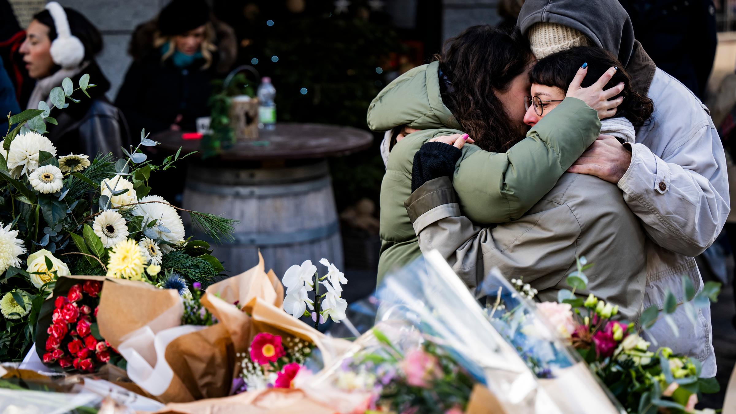 Menschen liegen sich am 02.01.2026 trauernd in den Armen vor niedergelegten Blumen, um den Opfern zu gedenken, die während der Neujahrsfeierlichkeiten in Crans-Montana durch einen Brand in der Schweizer Bar und Lounge „Le Constellation” ums Leben kamen und verletzt wurden. 