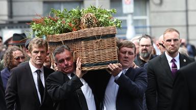 Sargträger tragen den Sarg von Glen Hansard während des Trauerzugs im Freien.