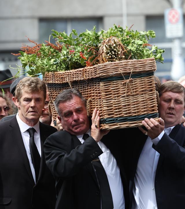 Sargträger tragen den Sarg von Glen Hansard während des Trauerzugs im Freien.