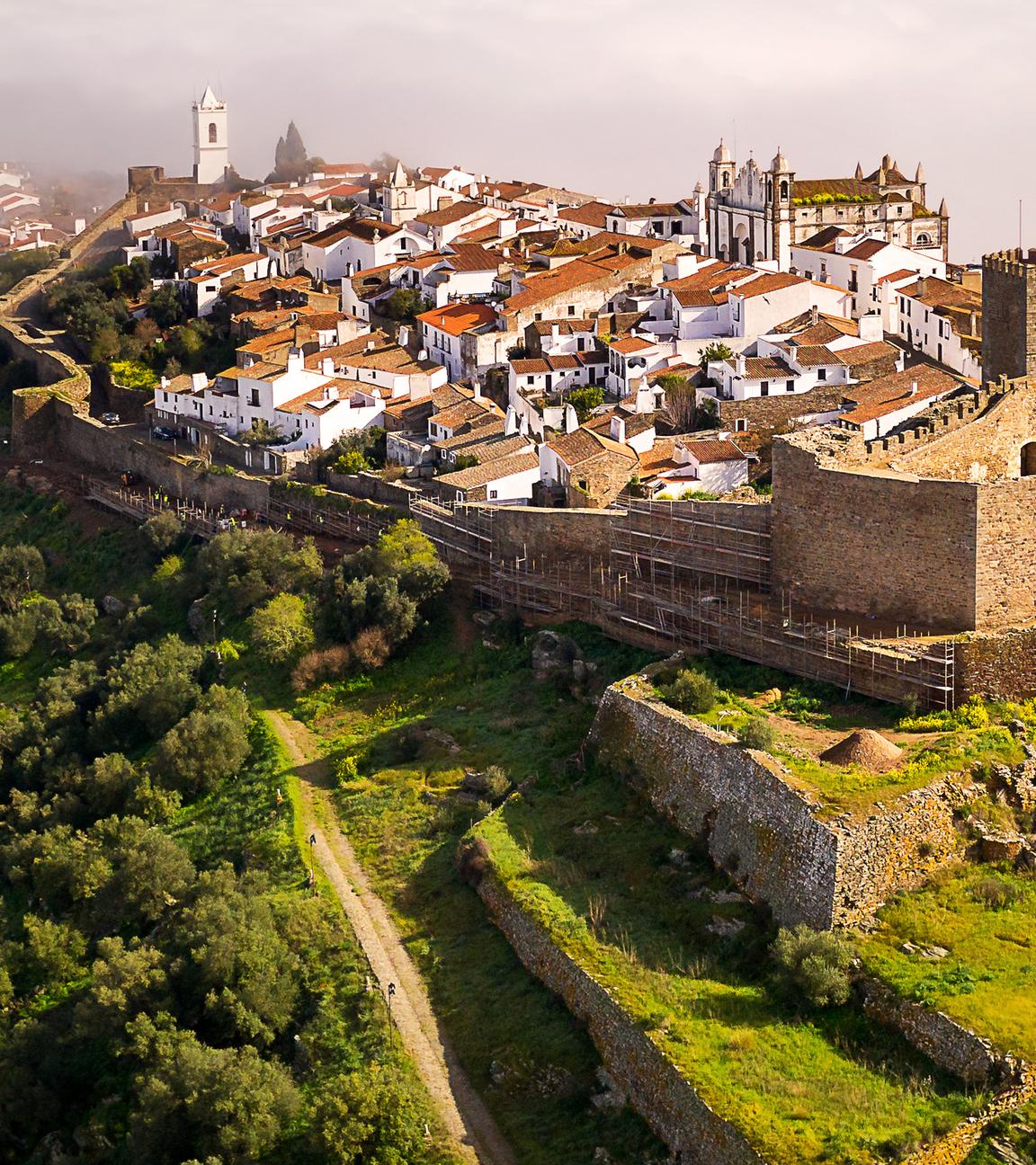 Luftaufnahme: Monsaraz liegt inmitten grüner Wiesen und Wälder im Morgennebel.