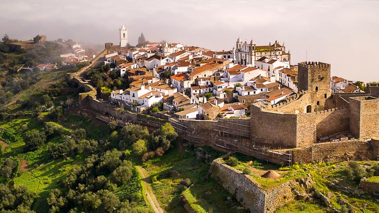  Luftaufnahme: Monsaraz liegt inmitten grüner Wiesen und Wälder im Morgennebel.