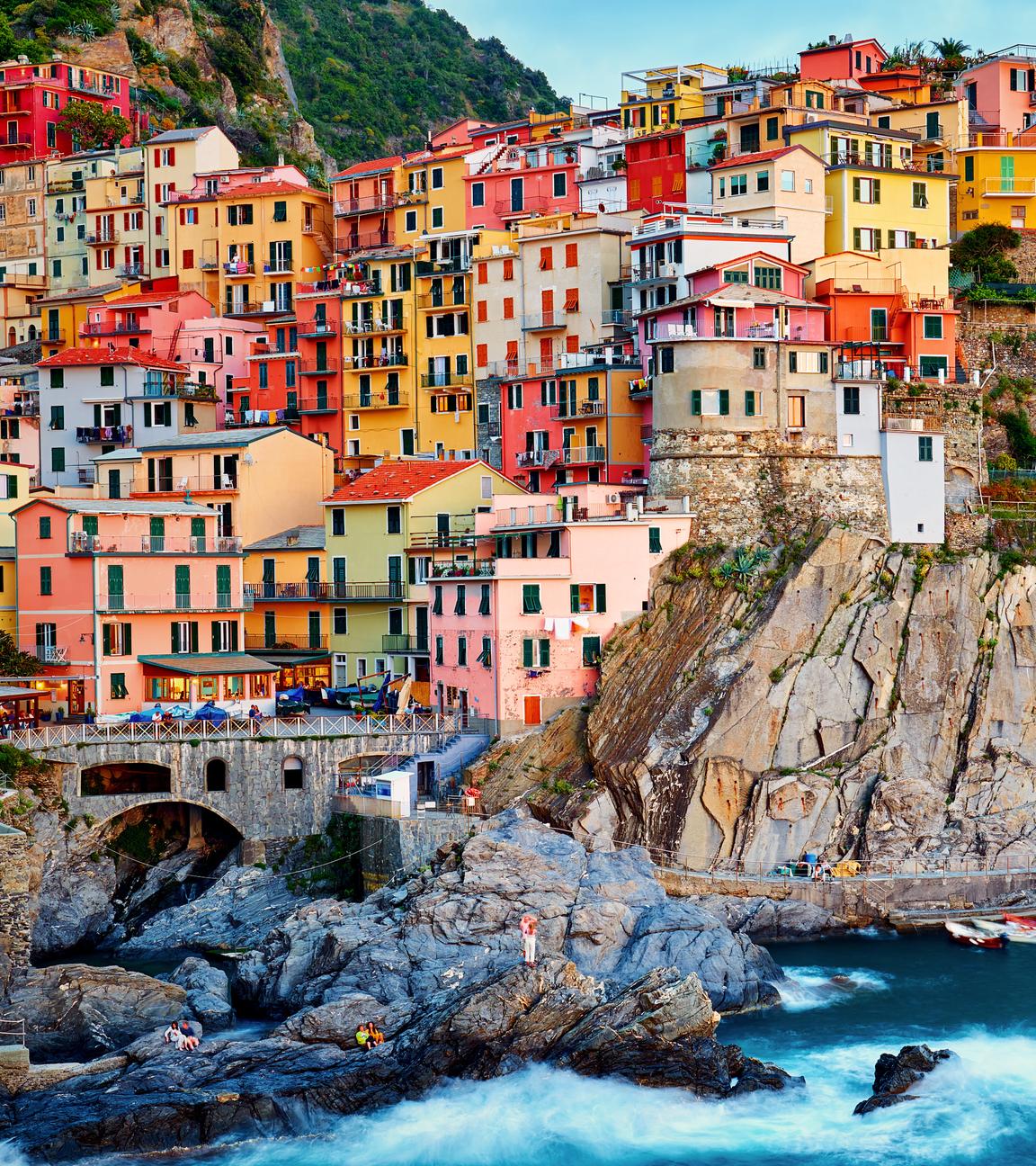Blick vom Meer aus auf ein Dorf, auf Manarola. Bunte Häuser schmiegen sich an eine steile, felsige Küste.