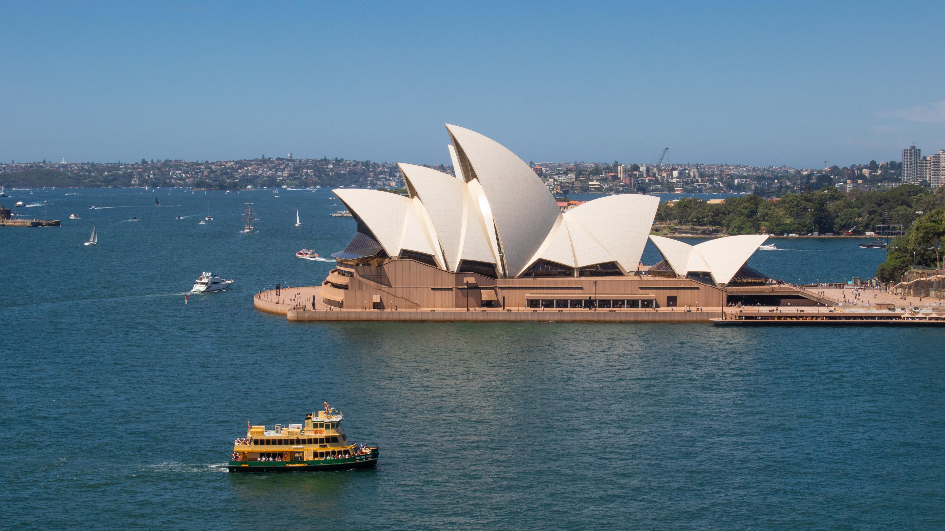 Panoramabild des Opernhauses von Sydney. Auf dem Wasser rund um das Gebäude sind mehrere Boote zu erkennen
